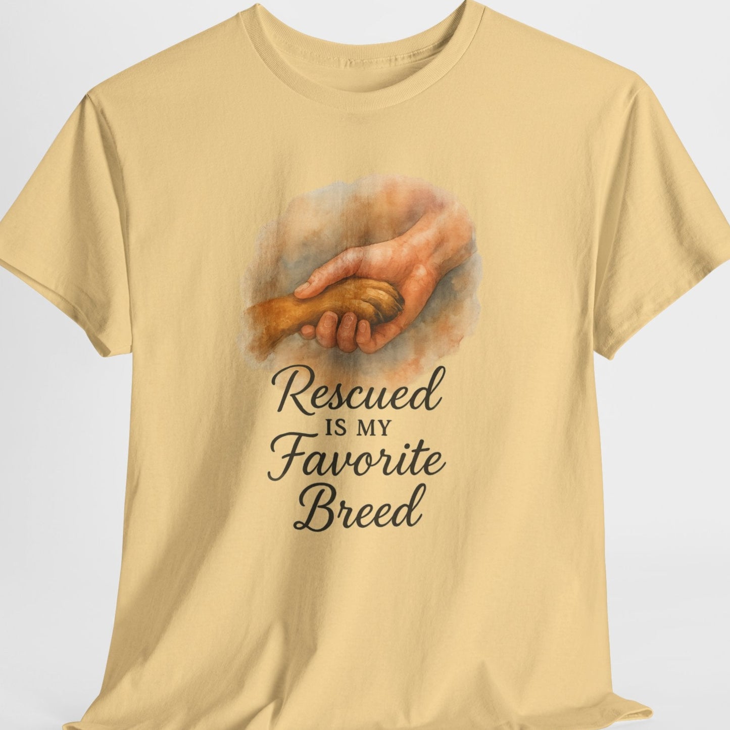 Beige t-shirt with a graphic of hands holding a dog and text 'Rescued is my Favorite Breed' on a light gray background