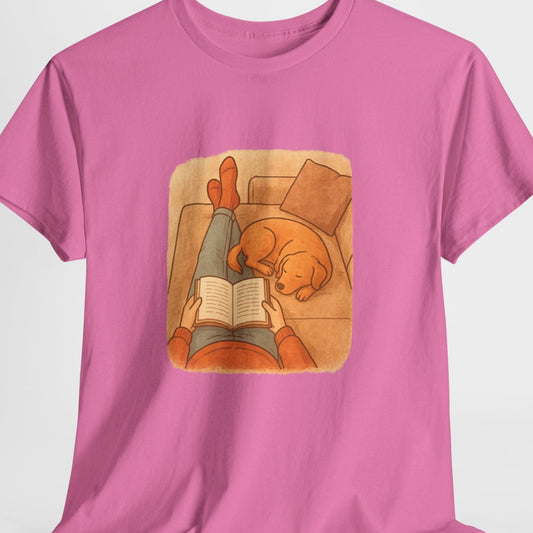 Pink t-shirt with a graphic of a person reading a book to a dog on a white background